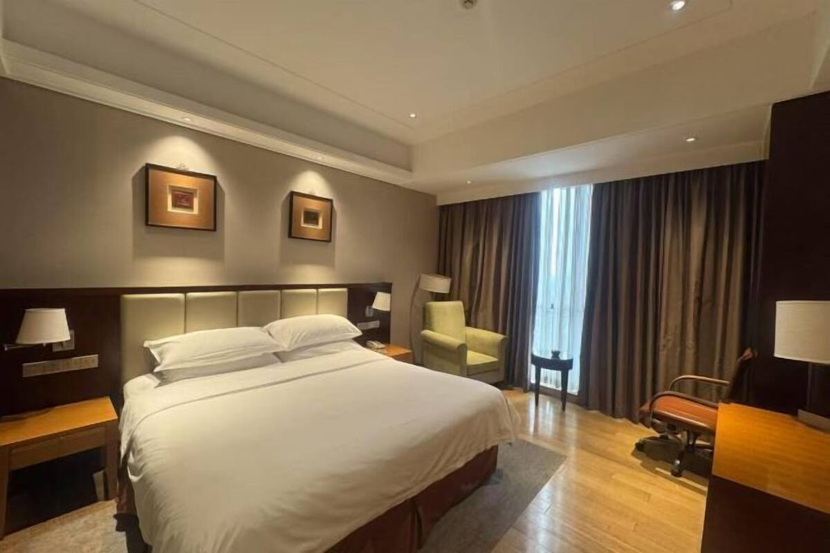 Habitación de hotel con una cama grande, dos mesitas de noche, una silla, un escritorio y una ventana con cortinas.