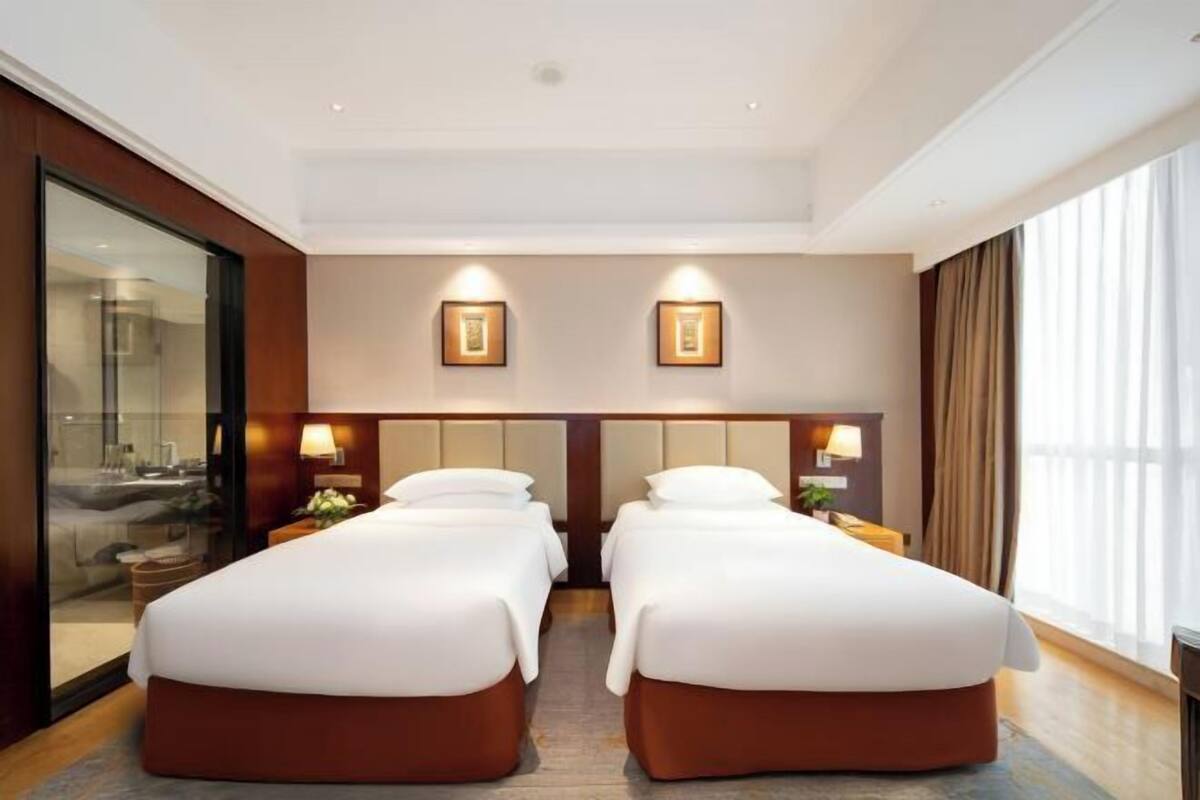 Habitación de hotel con dos camas, un separador de vidrio y vistas al exterior.