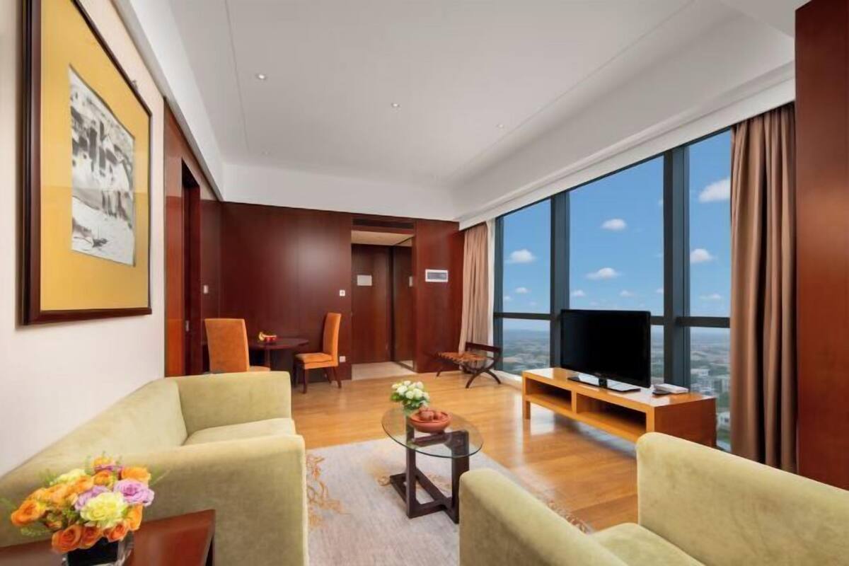 Habitación de hotel moderna con un ventanal grande, televisión de pantalla plana y una zona de estar con dos sofás y una mesa de centro.