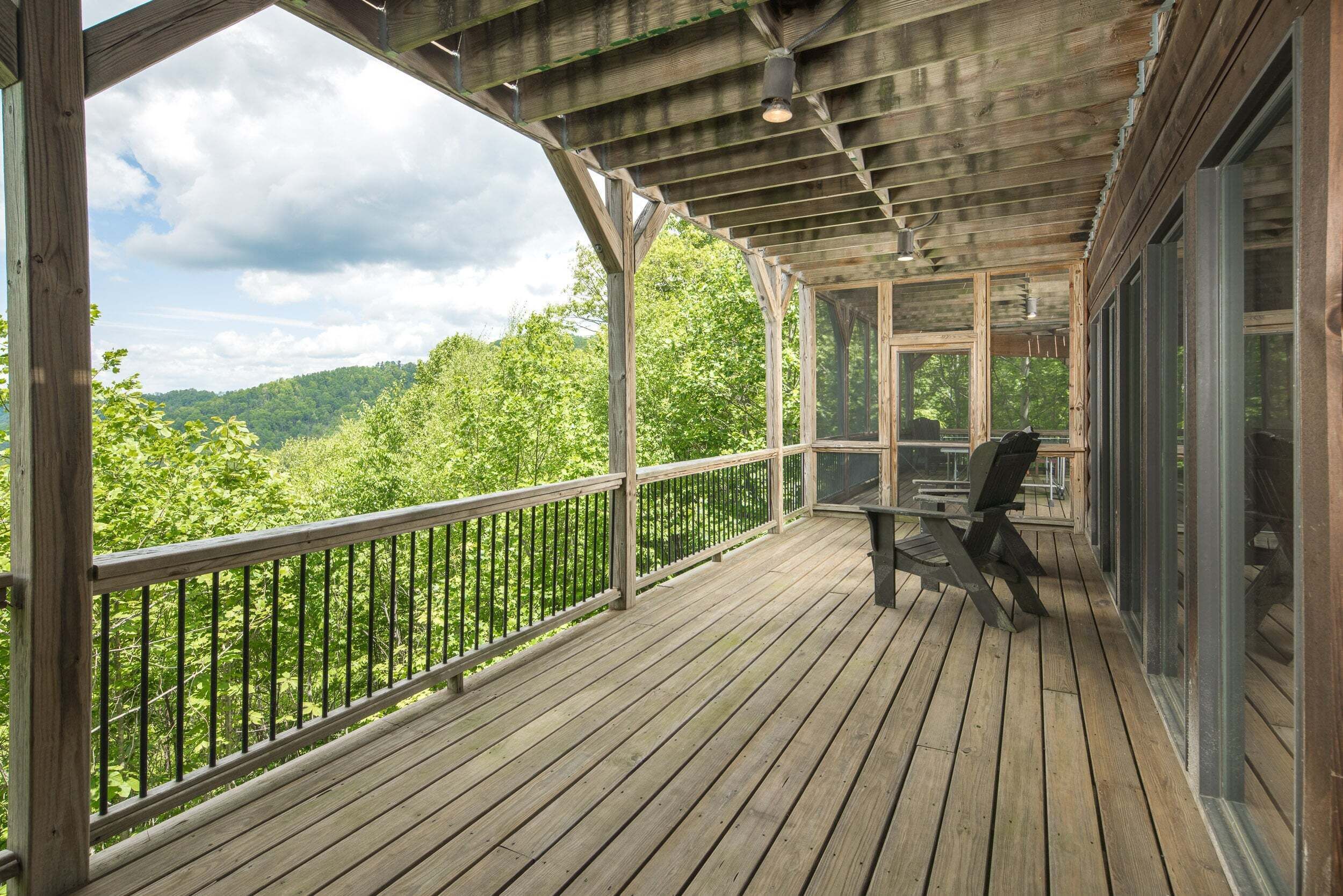 A wooden deck with a railing, a table, and chairs, overlooking a forested area.