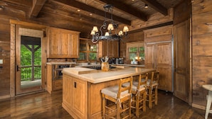A wooden cabin-style kitchen with a large island, bar stools, and a hanging light fixture. - Elegant Home with Incredible Views (Banner Elk)