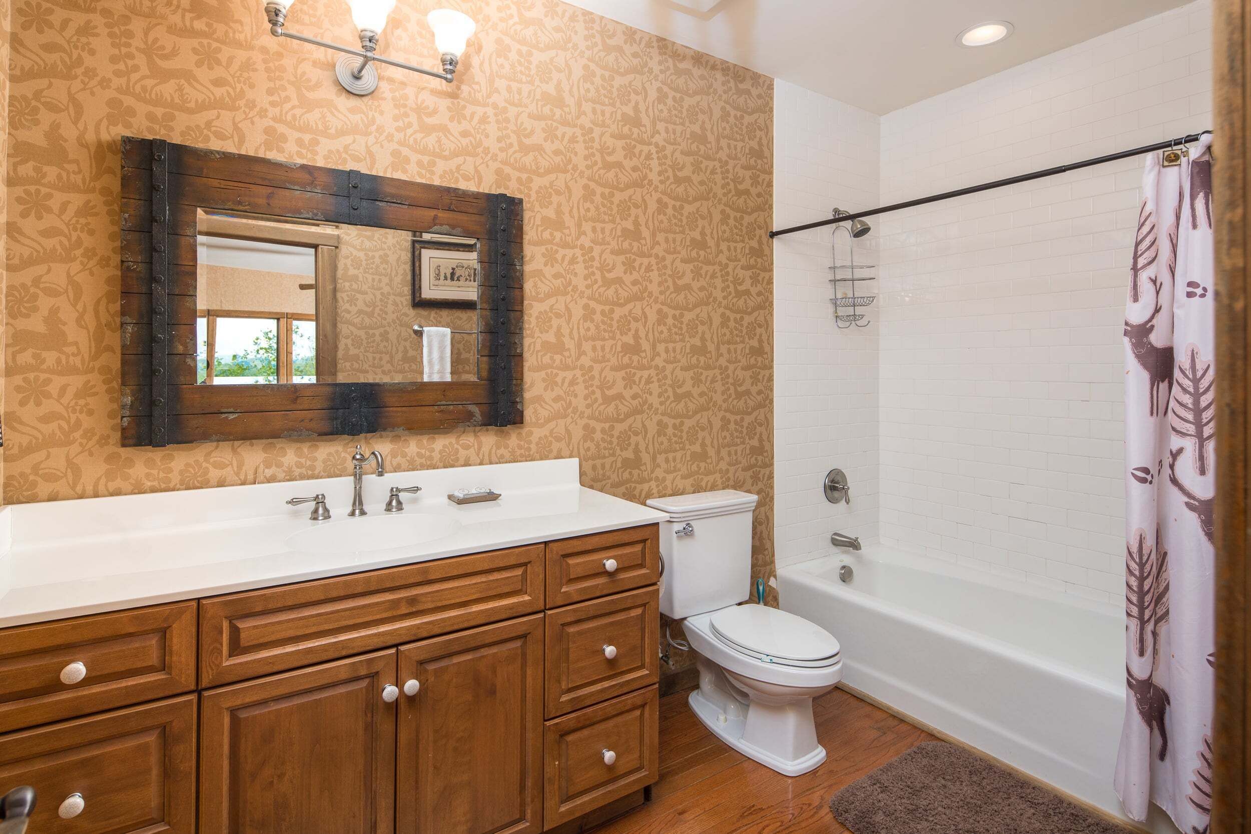 Une salle de bain avec un meuble-lavabo en bois, des toilettes blanches, une baignoire et un rideau de douche.