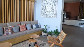 Een moderne woonkamer met een grijze bank, gestreepte kussens, een houten salontafel en twee rieten stoelen.