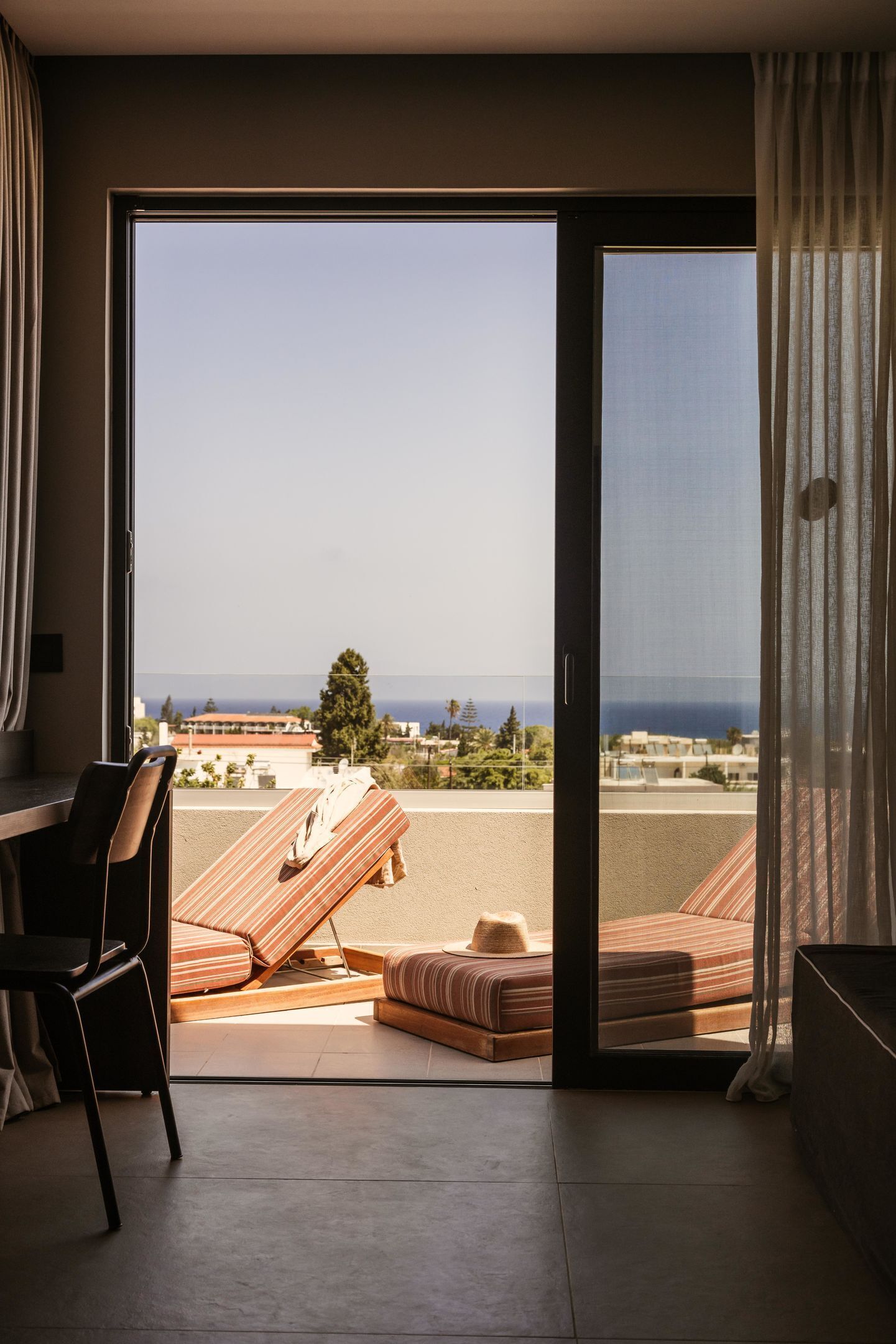 Una habitación con puerta de vidrio corredera que da a un balcón con vista al mar y edificios.