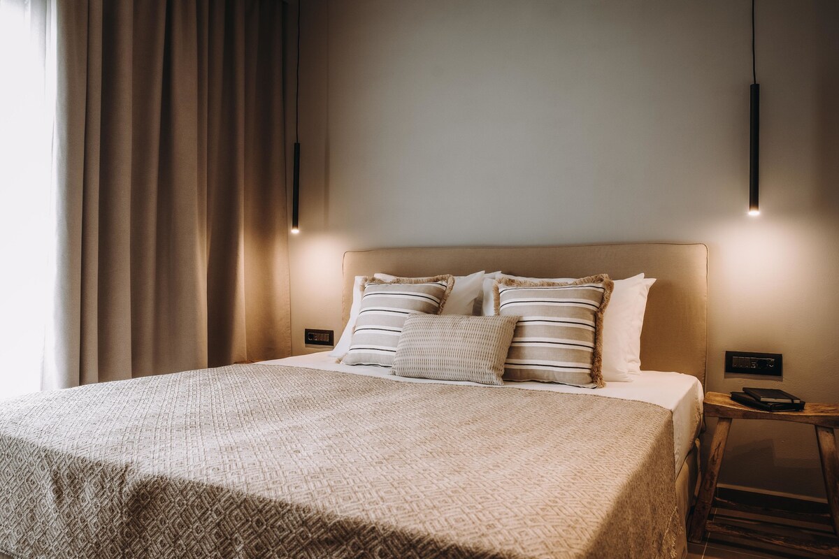 A neatly made bed with a patterned bedspread, two pillows, and a bedside table with a lamp.