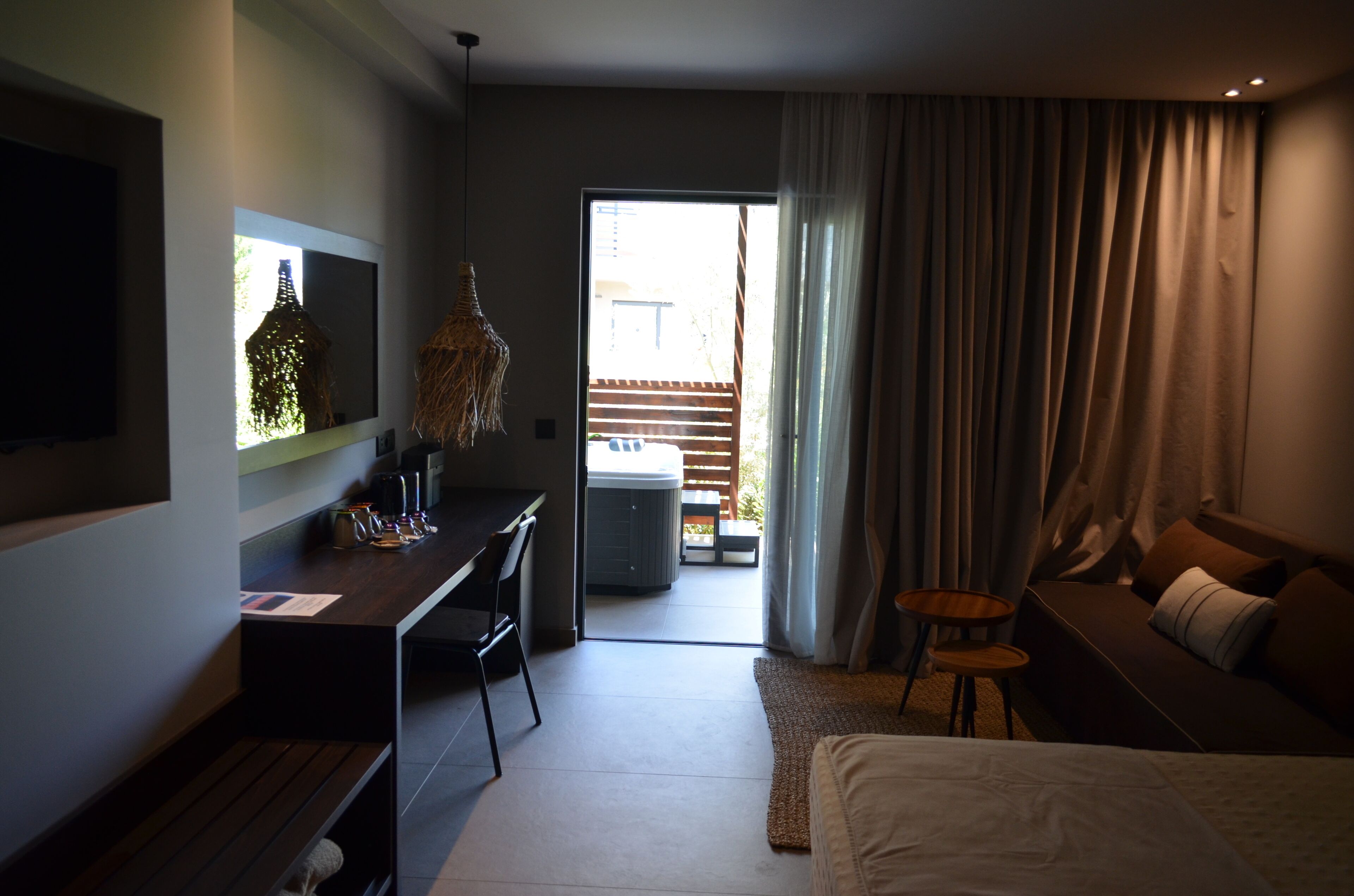 Una habitación de hotel moderna con una cama, un escritorio, una silla, un televisor y vistas al balcón exterior.