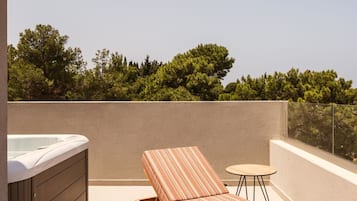 A rooftop terrace with a hot tub, a sun lounger, and a small table.
