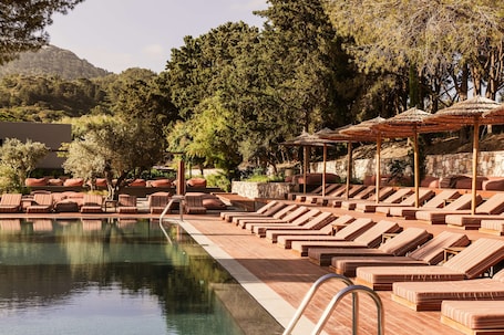 Una piscina al aire libre, sombrillas, sillones reclinables de piscina