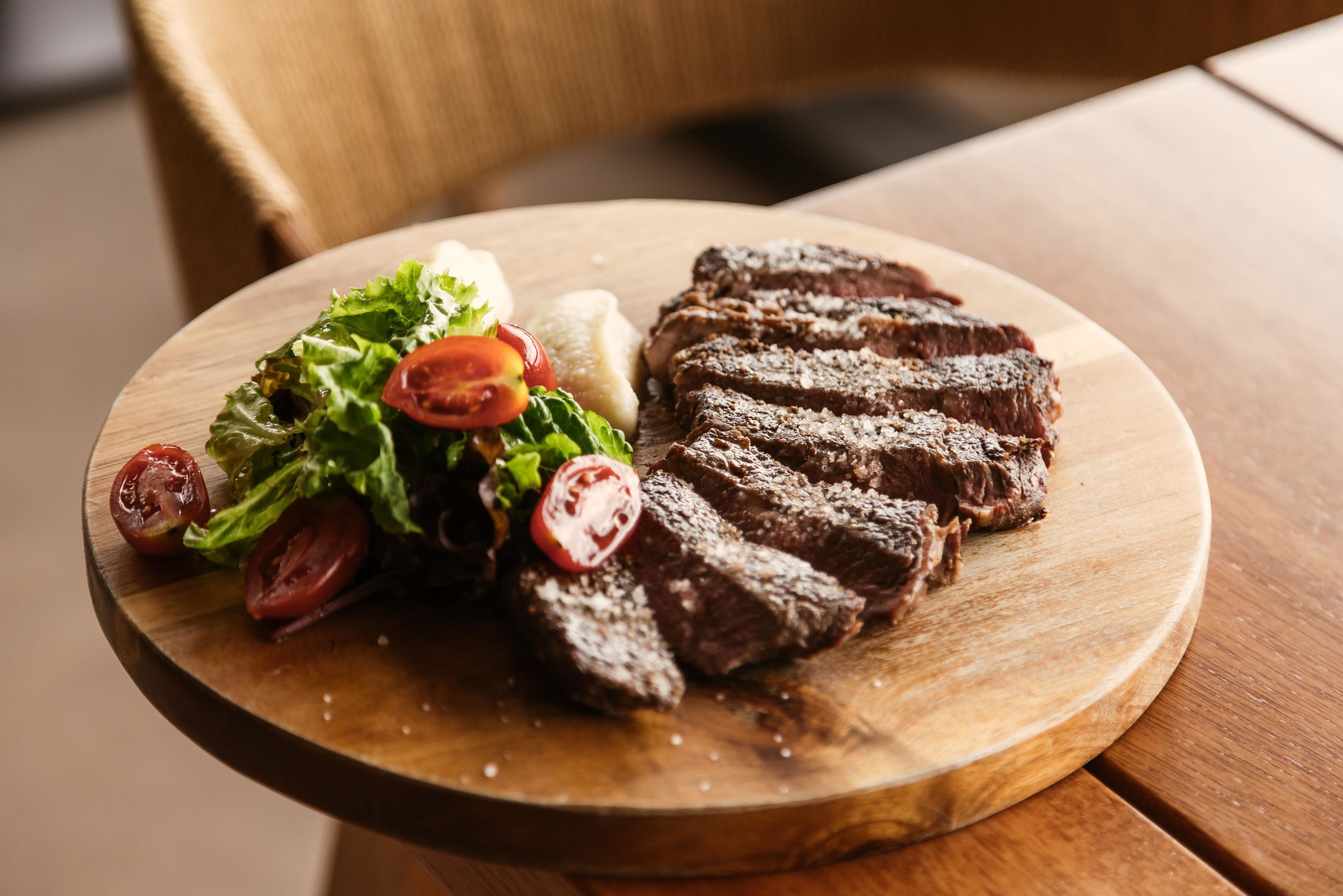 A wooden table with a plate of sliced steak and a salad.