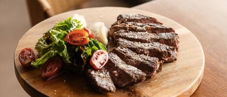 A wooden table with a plate of sliced steak and a salad.