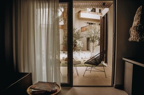 An open sliding door leading to a balcony with a chair and a small table.