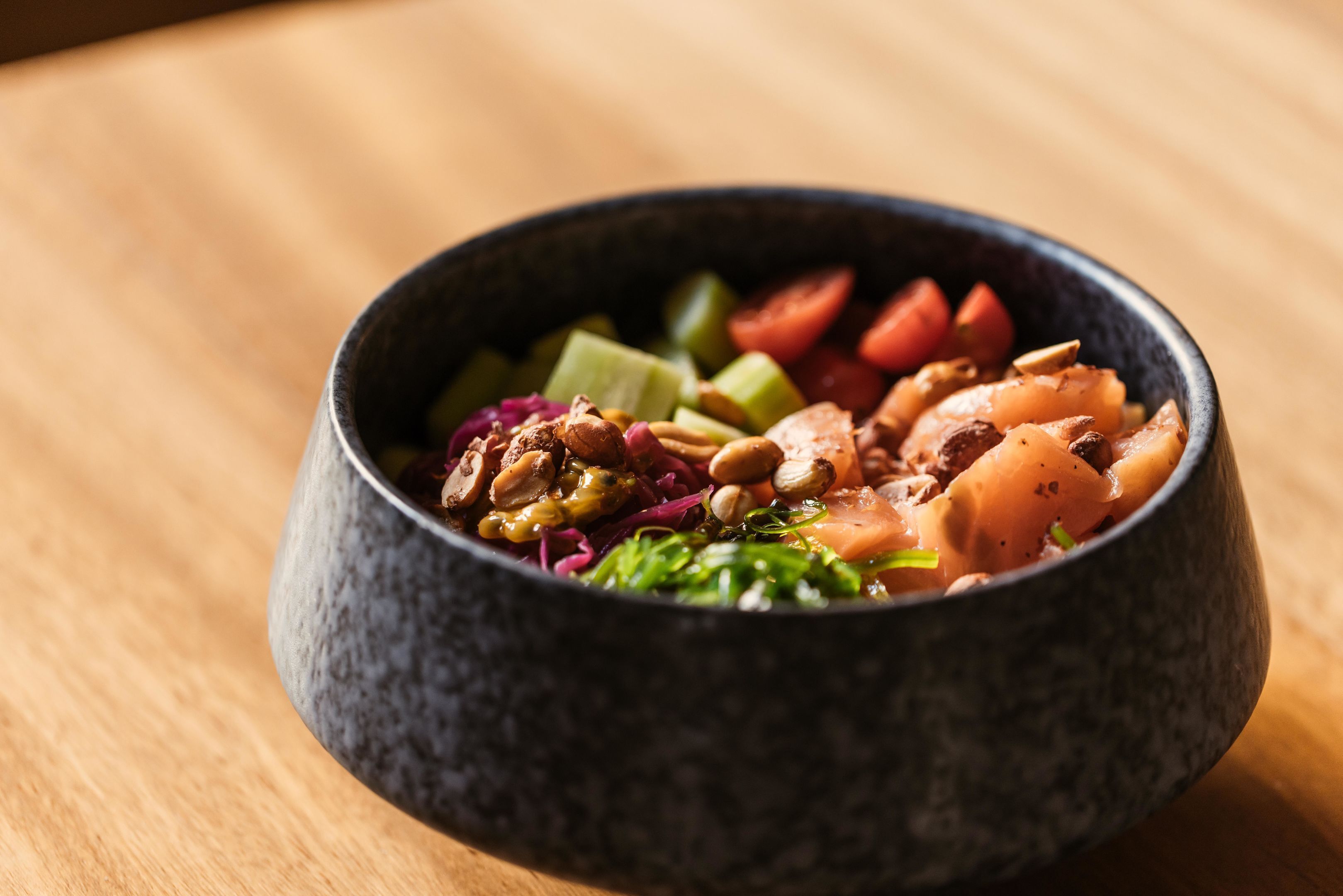 Un tazón de ensalada con diferentes verduras y nueces sobre una mesa de madera.