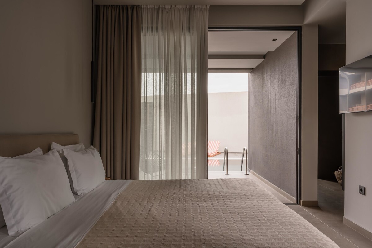 A modern hotel room with a large bed, a sliding glass door to a balcony, and a minimalist design.