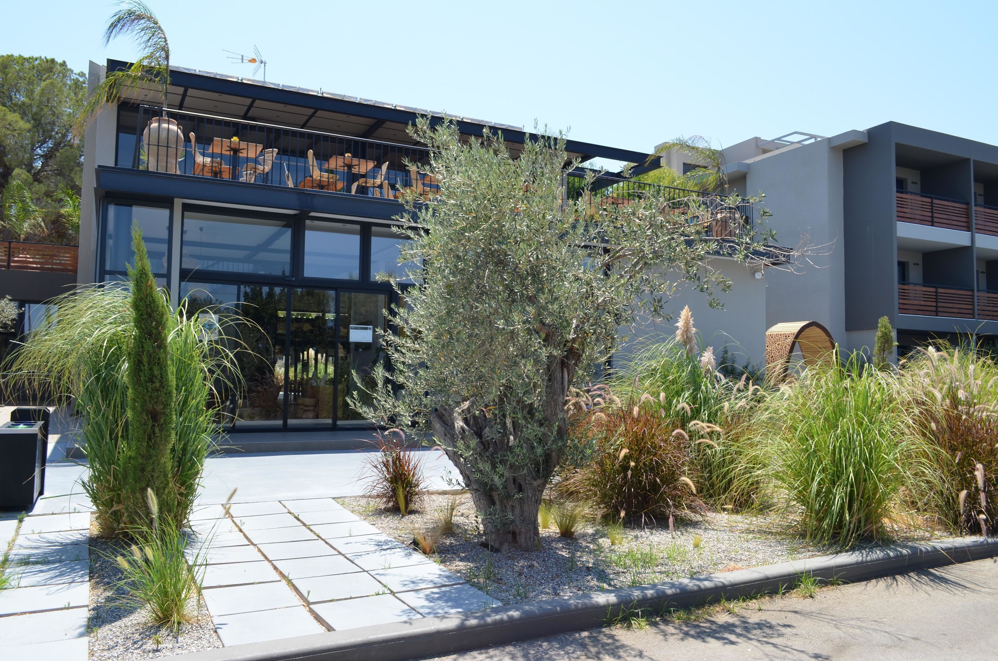 A modern building with a glass facade, outdoor seating area, and a variety of plants.