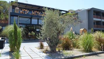 A modern building with a glass facade, outdoor seating area, and a variety of plants.