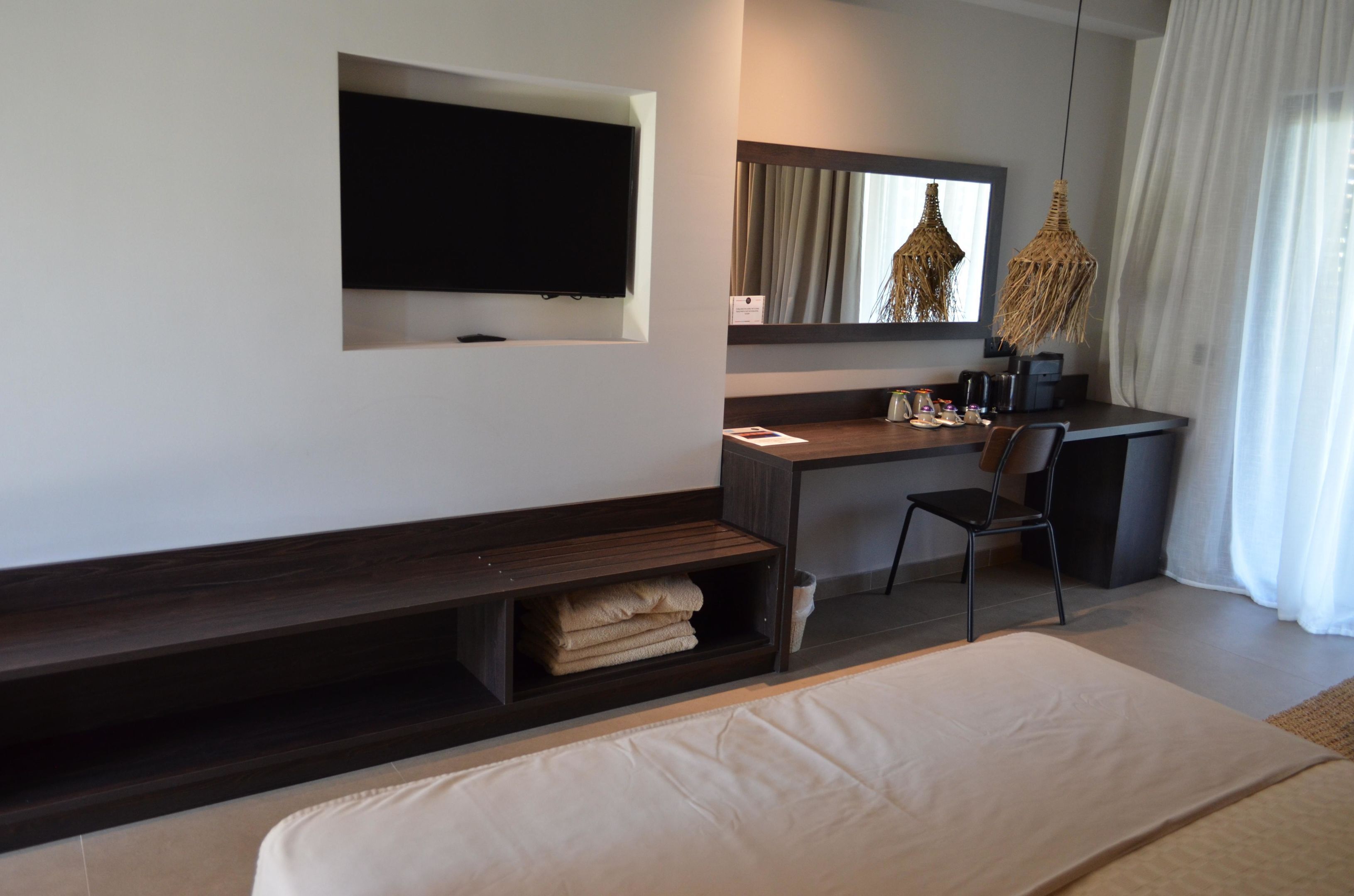 Una habitación de hotel moderna con televisión de pantalla plana en la pared, un escritorio con silla, una cama y un gran ventanal con cortinas.
