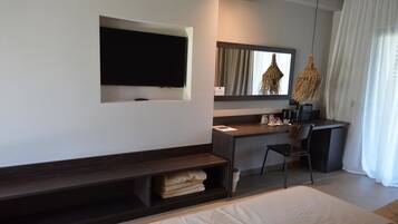 Una habitación de hotel moderna con televisión de pantalla plana en la pared, un escritorio con silla, una cama y un gran ventanal con cortinas.