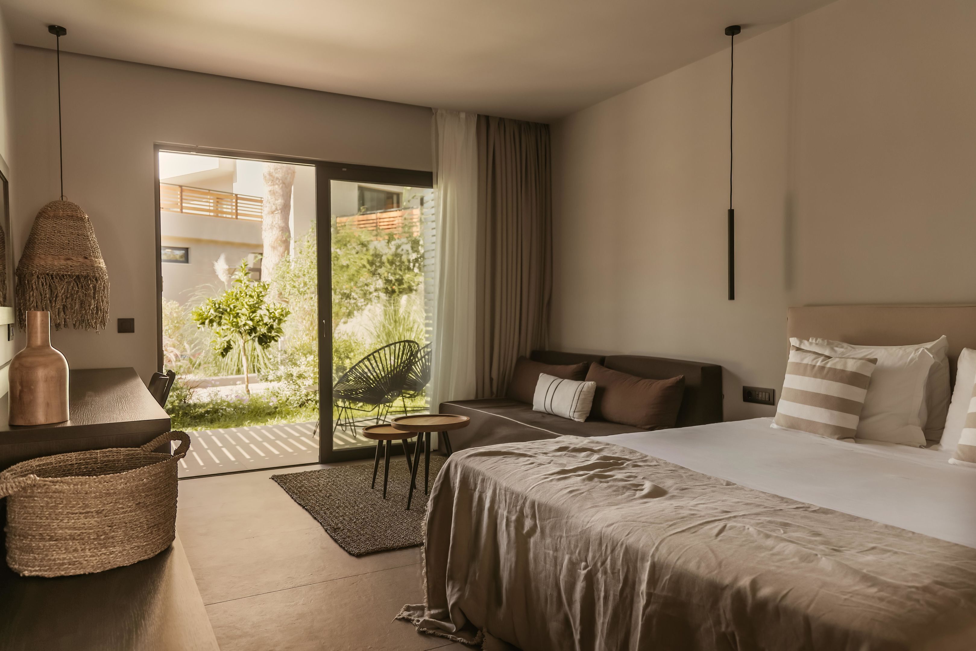 Habitación de hotel moderna con una cama grande, un escritorio, una silla y vistas a un jardín a través de una puerta corredera.