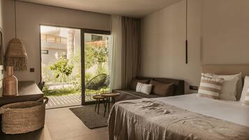 Habitación de hotel moderna con una cama grande, un escritorio, una silla y vistas a un jardín a través de una puerta corredera.