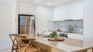 Una cocina moderna con armarios blancos, un refrigerador de acero inoxidable, una encimera de granito y un horno empotrado.