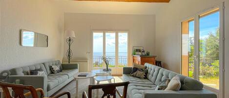A living room with a sofa, chairs, a coffee table, and a view of the sea through large windows.