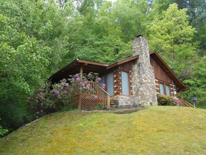A rustic cabin with a stone chimney, wooden deck, and surrounded by lush greenery. - Falling Waters | Secluded Cabin Not Far From the Parkway in Pigeon Forge (Pigeon Forge)