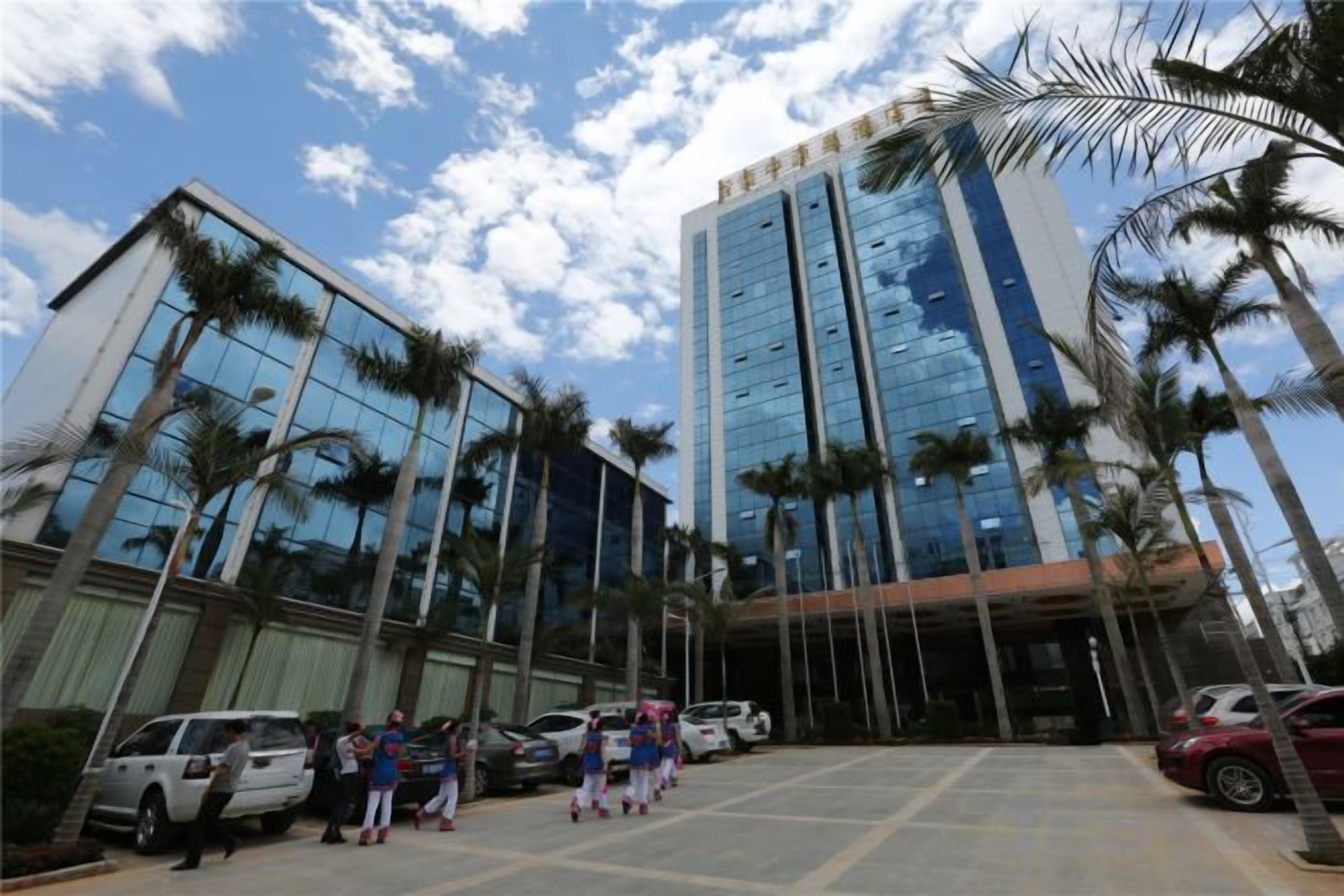 Un edificio moderno con fachada de vidrio, palmeras y automóviles estacionados.
