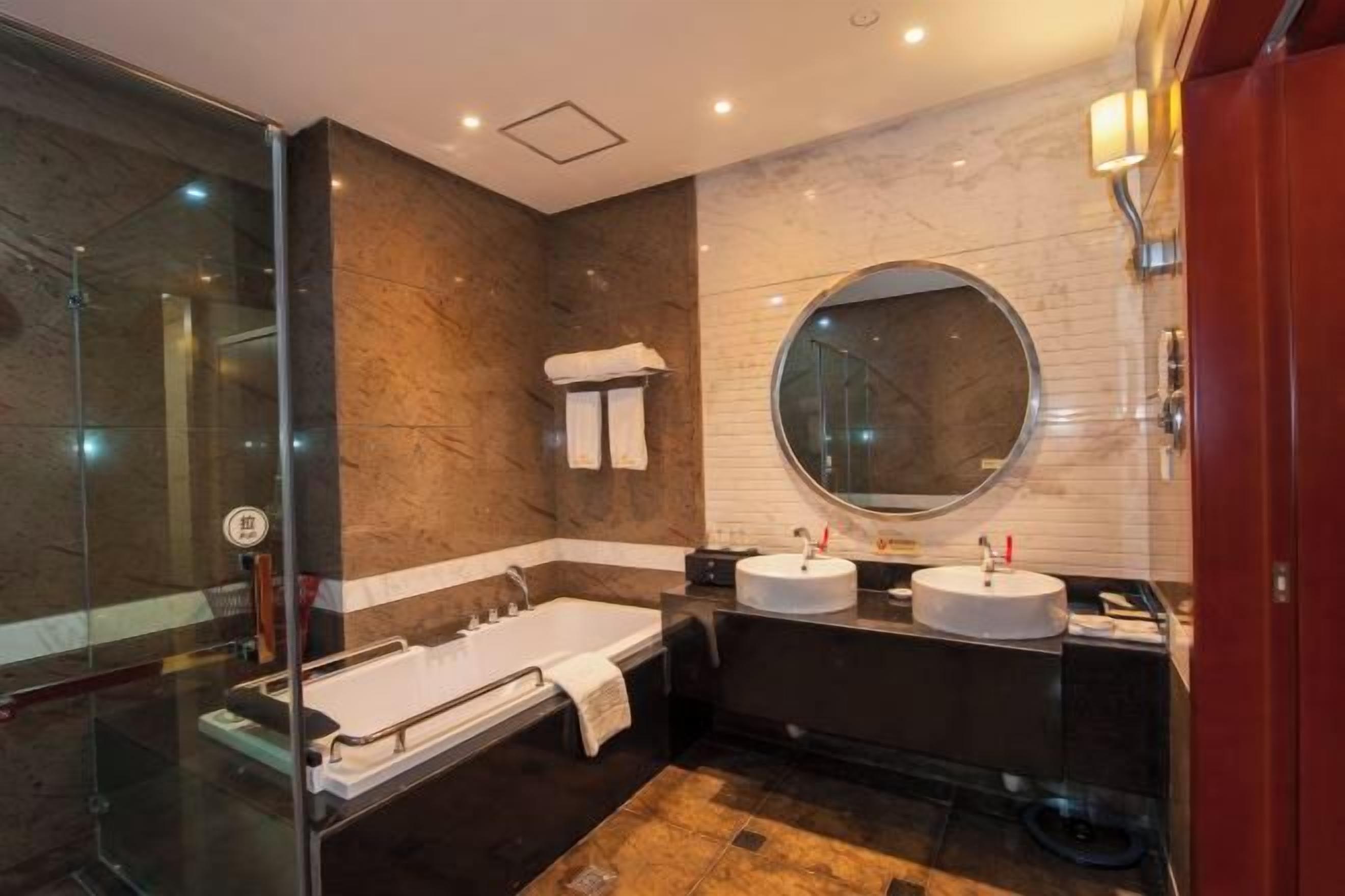 Une salle de bain moderne avec une douche à parois de verre, un grand miroir rond, deux vasques et une baignoire.