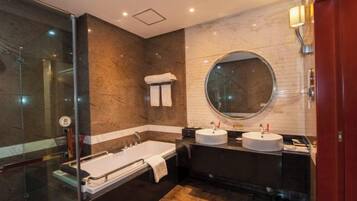 Une salle de bain moderne avec une douche à parois de verre, un grand miroir rond, deux vasques et une baignoire.