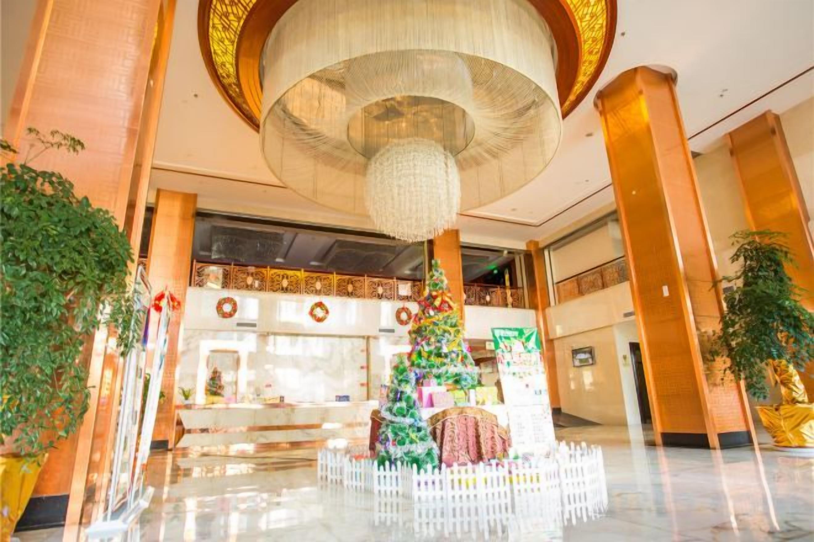 A lobby with a large chandelier, a Christmas tree, and a reception desk.