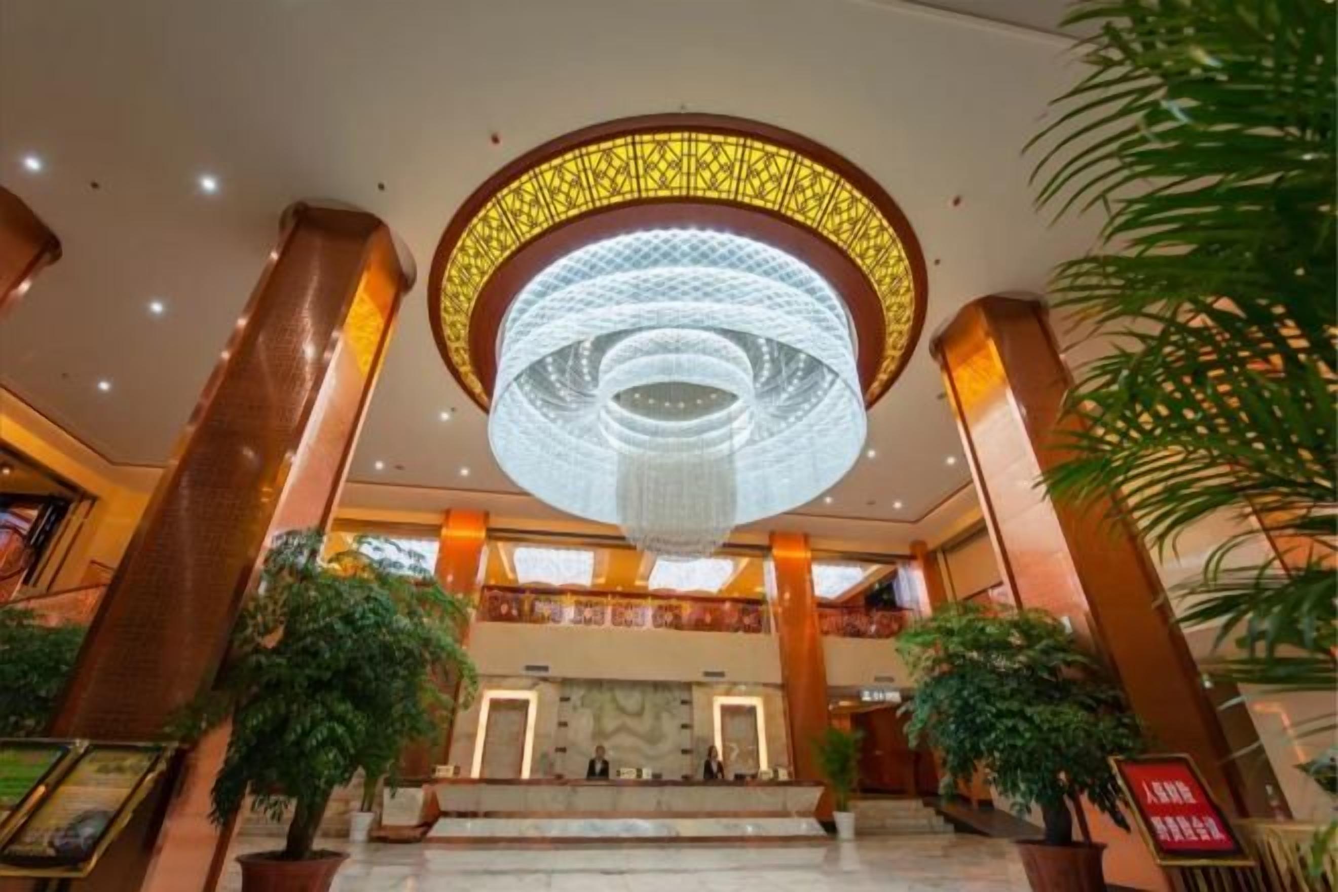 A lobby with a large circular chandelier, marble flooring, and potted plants.
