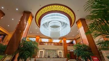 A lobby with a large circular chandelier, marble flooring, and potted plants.