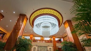 Een hotellobby met een grote, ronde kroonluchter, marmeren vloeren en potplanten.