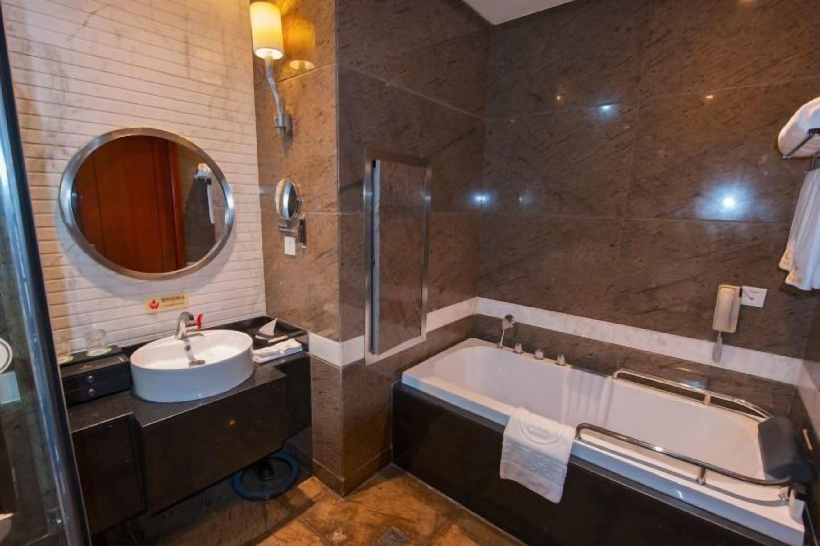 A modern bathroom with a round mirror, a sink, a bathtub, and a shower.