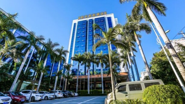 Een modern hotel met een hoge, glazen gevel en palmbomen op de voorgrond.