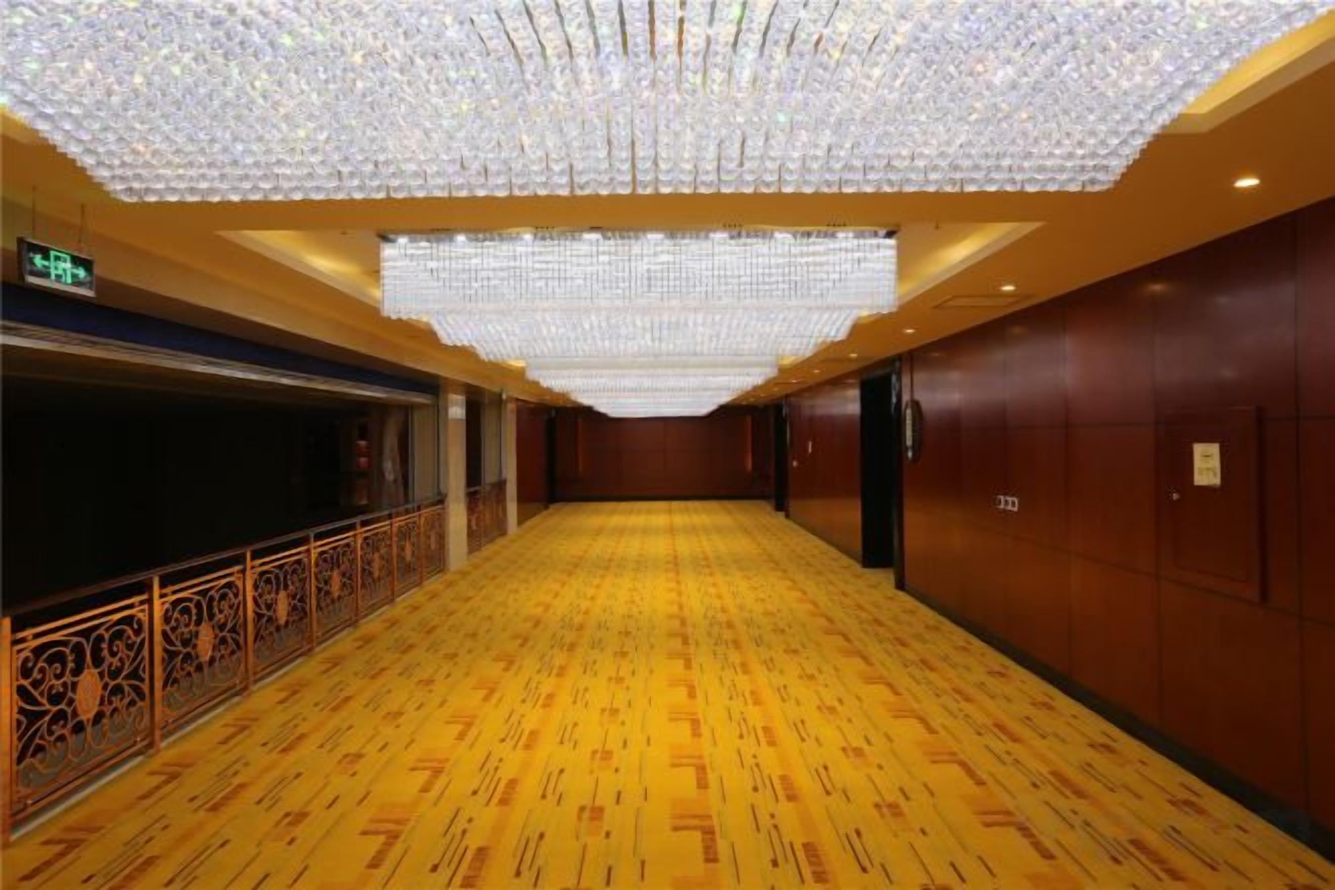 A hotel corridor with a patterned floor, a decorative railing, and a ceiling with hanging lights.