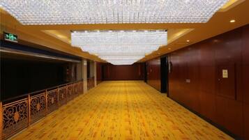 A hotel corridor with a patterned floor, a decorative railing, and a ceiling with hanging lights.
