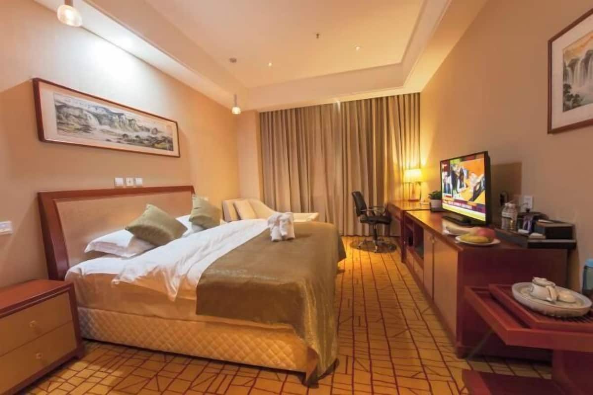 A hotel room with a bed, a desk, a television, and a painting on the wall.
