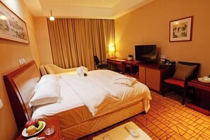 Ein Hotelzimmer mit Bett, Schreibtisch mit Stuhl, Fernseher und Essbereich mit Obstteller.