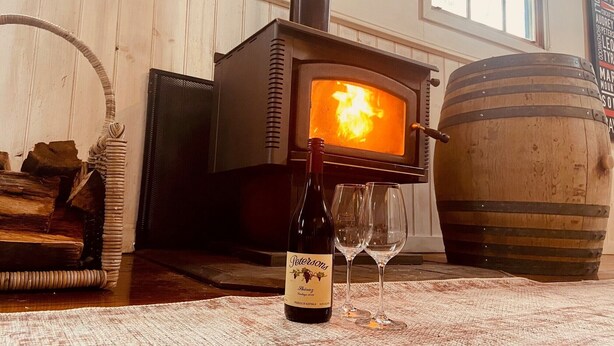 Une pièce avec un poêle à bois, une bouteille de vin et deux verres posés sur une table.
