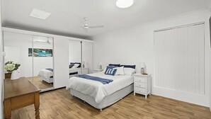 A bedroom with a bed, bedside table, nightstand, mirror, and a wooden desk.