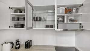 A kitchen with open cabinets displaying cookware, a kettle, a toaster, and a coffee maker.