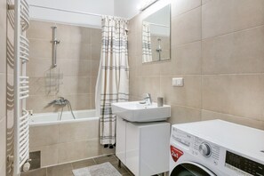 Een badkamer met een badkuip, douche, wastafel en een wasmachine.