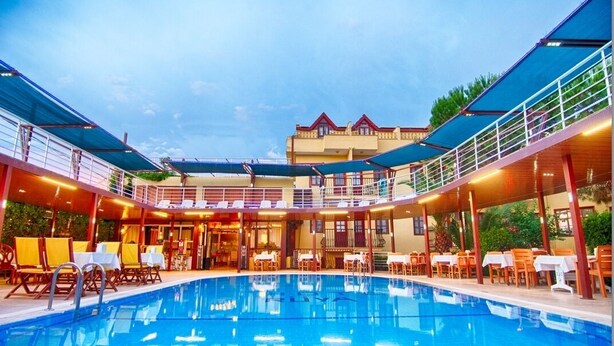 A pool area with a covered seating area and a building in the background. - GARDEN RUYA HOTEL (Fethiye)