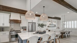 A spacious kitchen with white cabinetry, a large island, and wicker chairs. - Stunning, Pet-Friendly,Beach Home Beside Dune Pool w/Extra Amenities Nearby (Port Aransas)
