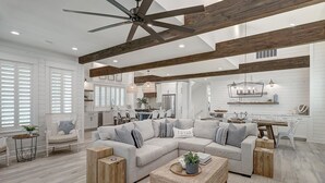 A spacious living room with a large L-shaped sectional sofa, wooden beams on the ceiling, and a modern kitchen in the background. - Stunning, Pet-Friendly,Beach Home Beside Dune Pool w/Extra Amenities Nearby (Port Aransas)