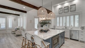 A spacious kitchen with a large island, white cabinetry, and a dining area with wicker chairs. - Stunning, Pet-Friendly,Beach Home Beside Dune Pool w/Extra Amenities Nearby (Port Aransas)
