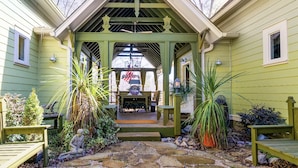 A covered porch with a table and chairs, surrounded by potted plants and a stone pathway.