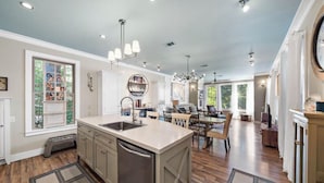 A spacious kitchen with a central island, large windows, and a dining area with a chandelier.