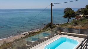 Une piscine dotée d’une balustrade en verre, une plage et une côte rocheuse.